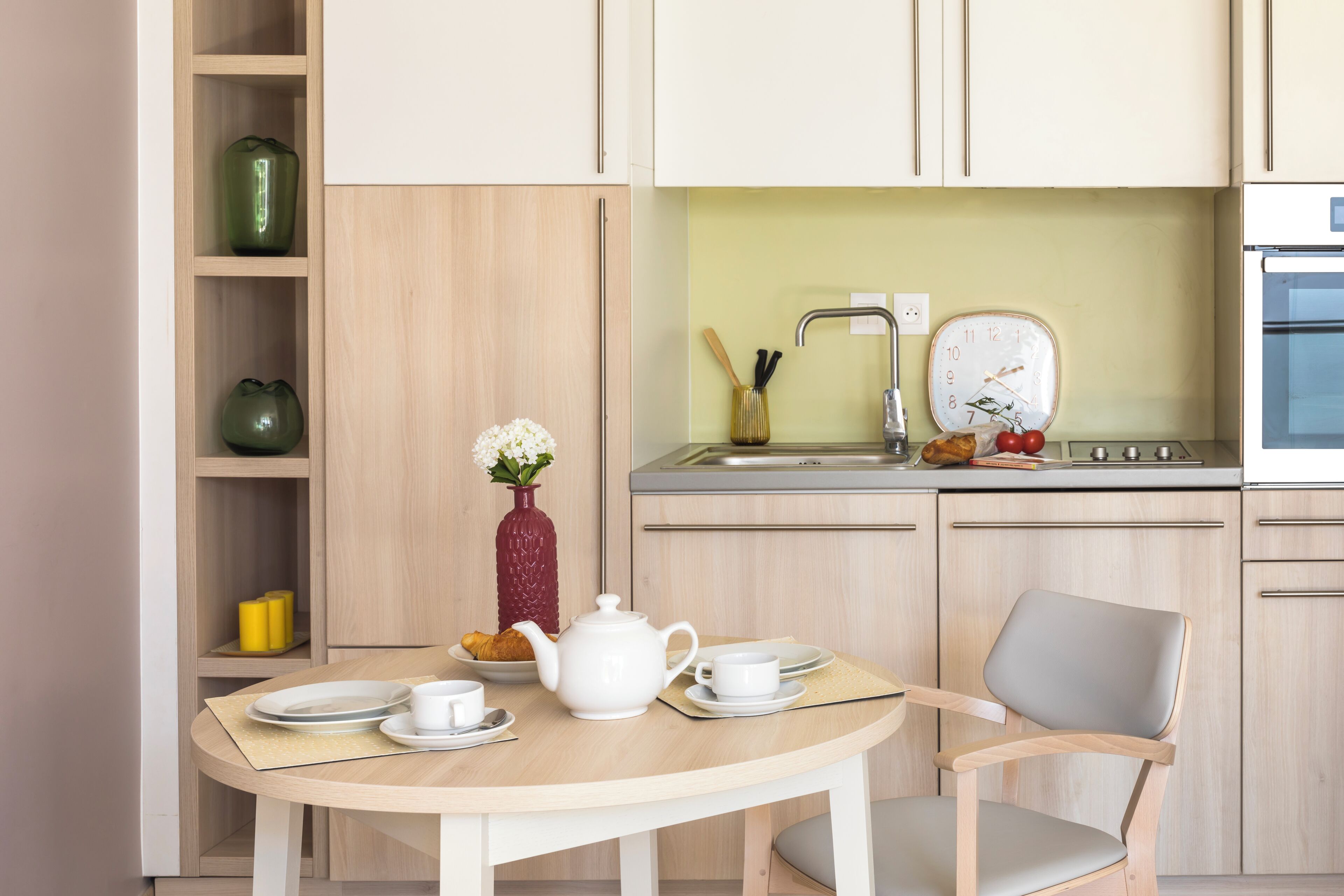 Una cocina moderna con una mesa de comedor, sillas, un lavamanos y un reloj.