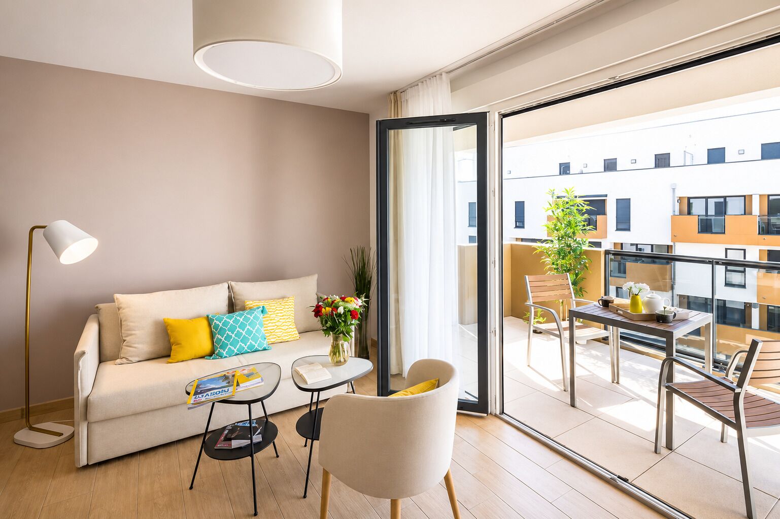 Un moderno salón con sofá, mesa de centro y sillas, un balcón con mesa y sillas, y vistas a la ciudad.