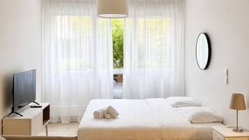 A hotel room with a bed, a TV, a sofa, a round table, and a view of greenery outside.