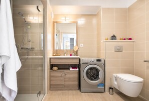 A modern bathroom with a glass shower enclosure, a built-in washing machine, and a toilet. - Zenao Appart'hôtels Lyon 7 (Lyon)