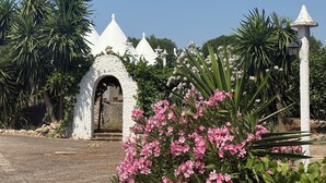 A white building with a stone archway, surrounded by lush greenery and pink flowers. - ALVICA  (Martina Franca)