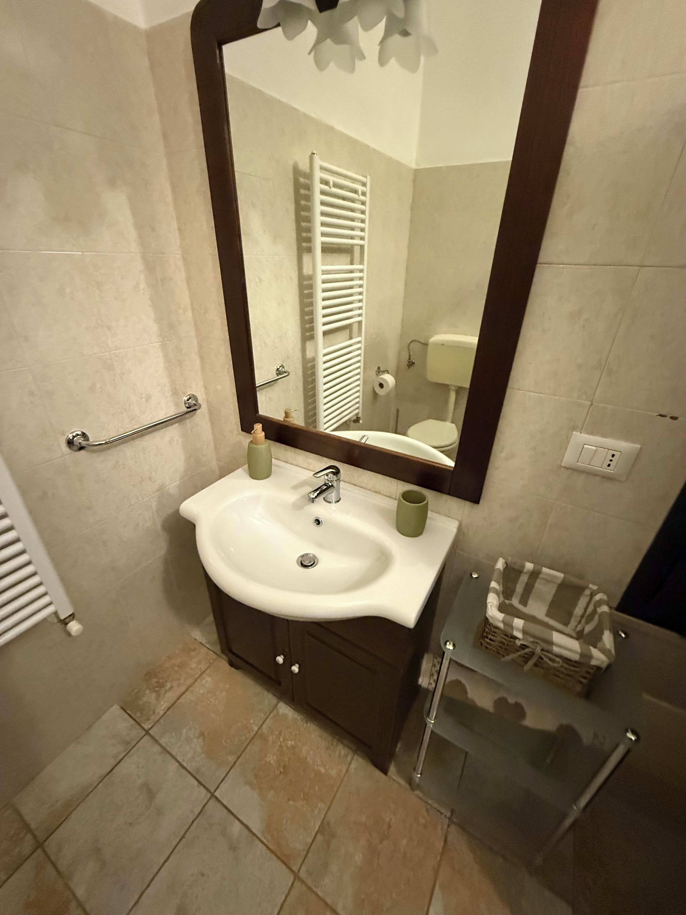 Une salle de bain avec un lavabo blanc, un miroir, un porte-serviettes et une étagère en verre sur laquelle se trouve un panier.