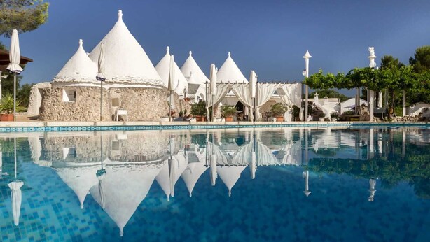 A pool with clear blue water, surrounded by white conical-roofed buildings and a white gazebo. - ALVICA  (Martina Franca)
