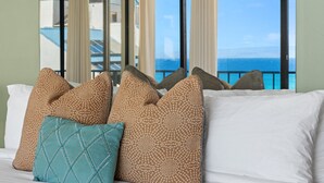 Een bed met gekleurde kussens en uitzicht op de oceaan door grote ramen.