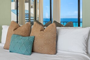 A bed with patterned pillows and a view of the ocean through large windows. - Ocean-view 1BR condo with pool, lanai, and full kitchen- Valley Isle 1001 (Lahaina)