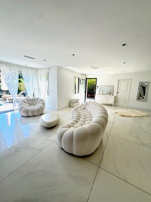 Ein modernes Wohnzimmer mit einem großen weißen Sofa, einem kleinen runden Hocker und einem einzigartigen, abgerundeten Couchtisch.