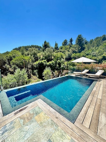 A rectangular swimming pool with a wooden deck and lounge chairs, surrounded by lush greenery and trees.. Holiday Home 'Alyana at the Foot of the Mountain' with Mountain View, Wi-Fi & Air Conditioning