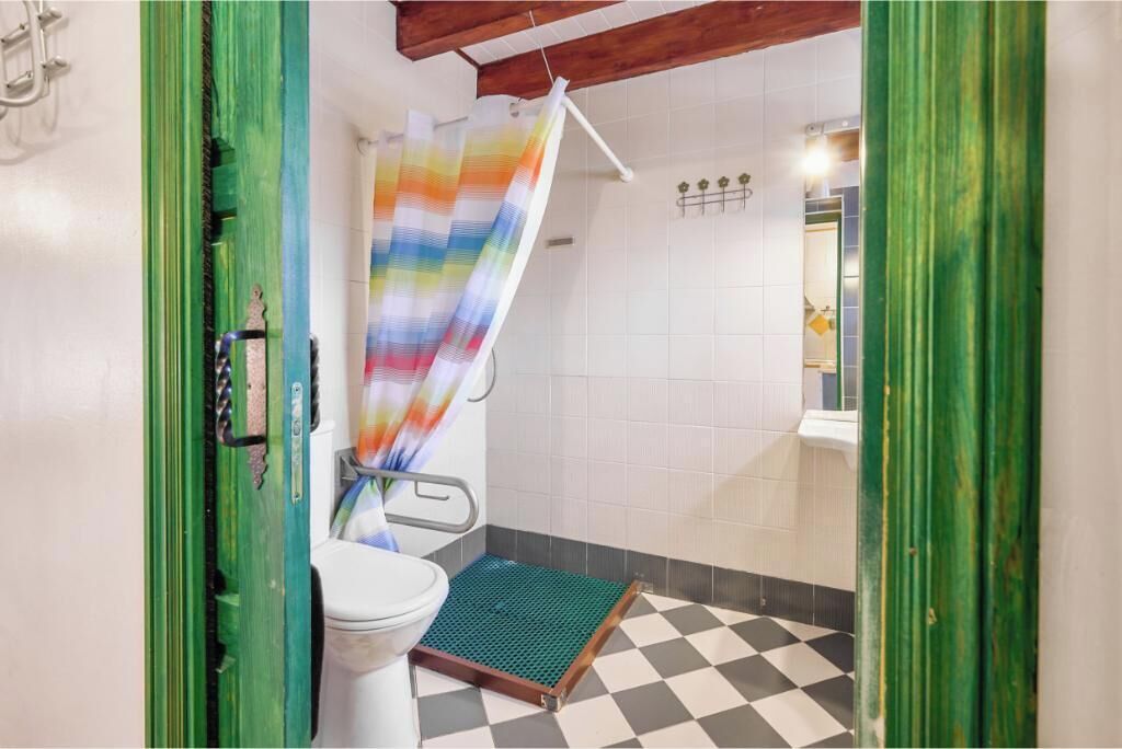 Une salle de bain équipée d’une douche accessible aux personnes en fauteuil roulant, de toilettes et d’un carrelage à motifs à carreaux.