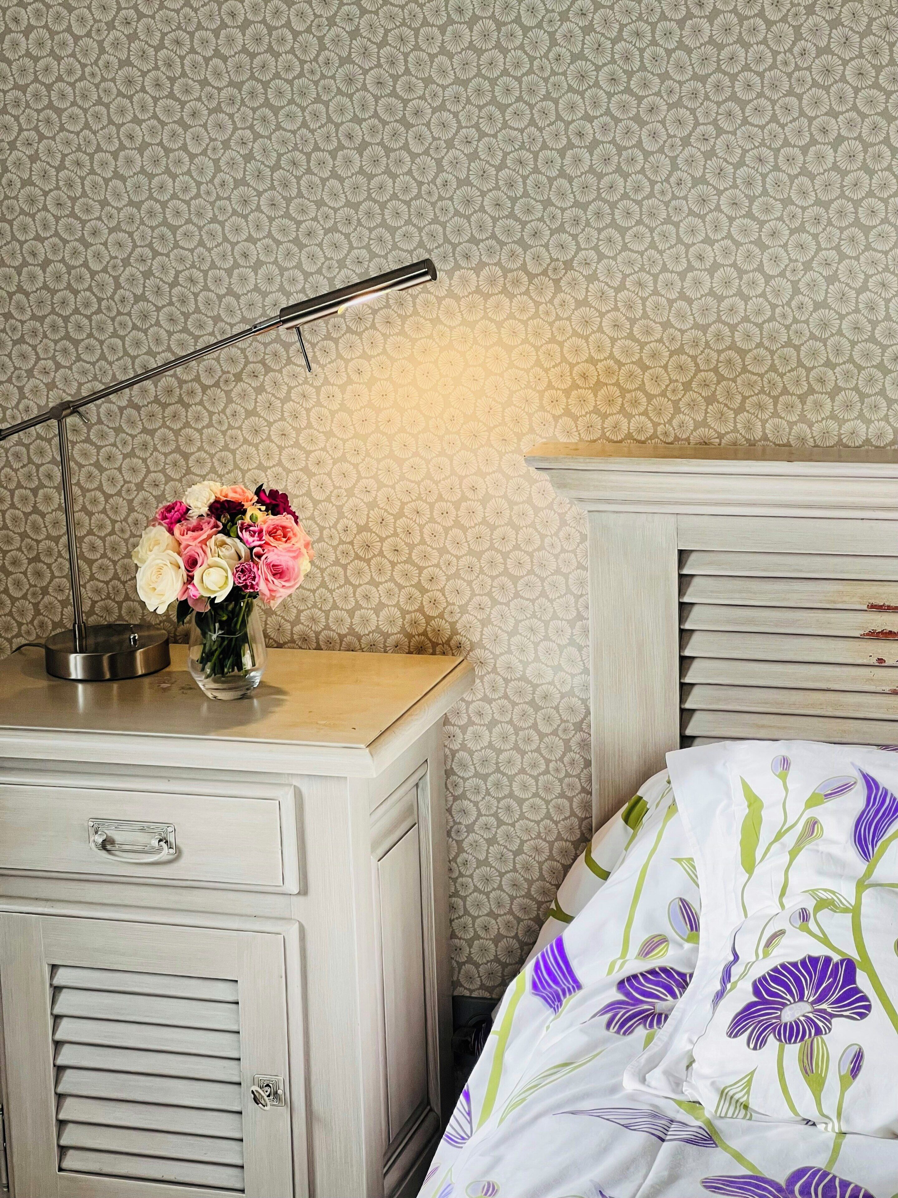 A bedroom with a bed, a nightstand, a lamp, and a vase with flowers.