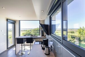 A modern kitchen with a large window, a coffee machine, and a dining area with chairs. - Villa with spa and sea view in Finistère (Goulven)