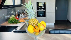 Une cuisine moderne avec un saladier en verre rempli de fruits posé sur le comptoir, une fenêtre et une porte.
