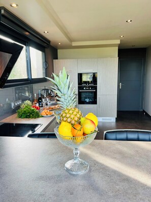 A modern kitchen with a glass bowl of fruit on the counter, a window, and a door. - Villa with spa and sea view in Finistère (Goulven)