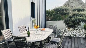 Un espace de restauration en plein air avec une table ronde et des chaises, une bouteille et un saladier de fruits.