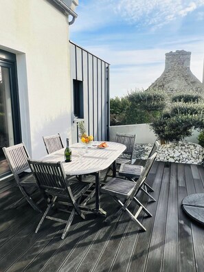 An outdoor dining area with a round table and chairs, a bottle, and a bowl of fruit. - Villa with spa and sea view in Finistère (Goulven)