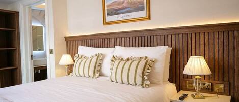 A hotel room with a large bed, two bedside lamps, a framed picture on the wall, and a wooden headboard.