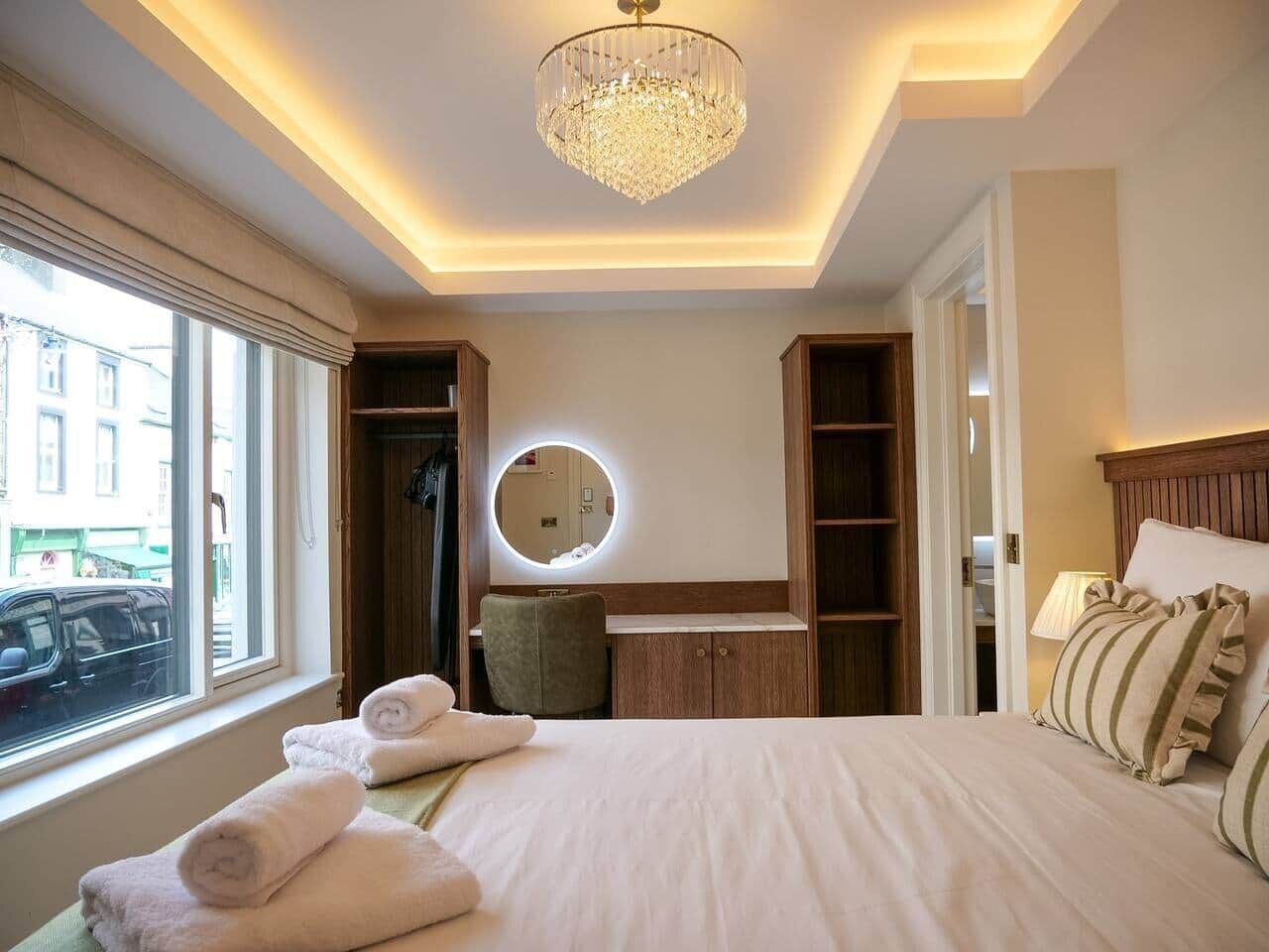 Quarto de hotel com uma cama grande, um espelho redondo, toucador e vista para a rua.