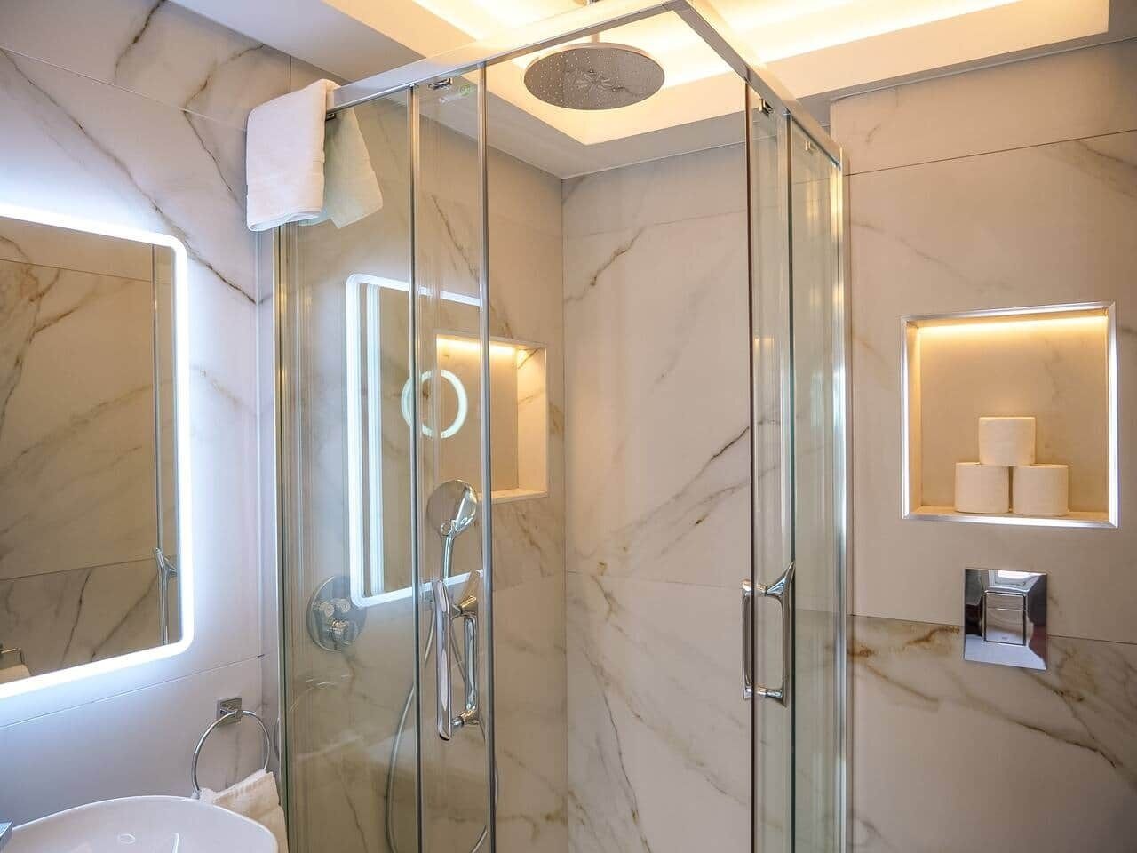 A modern bathroom with a glass-enclosed shower, marble walls, and built-in lighting.