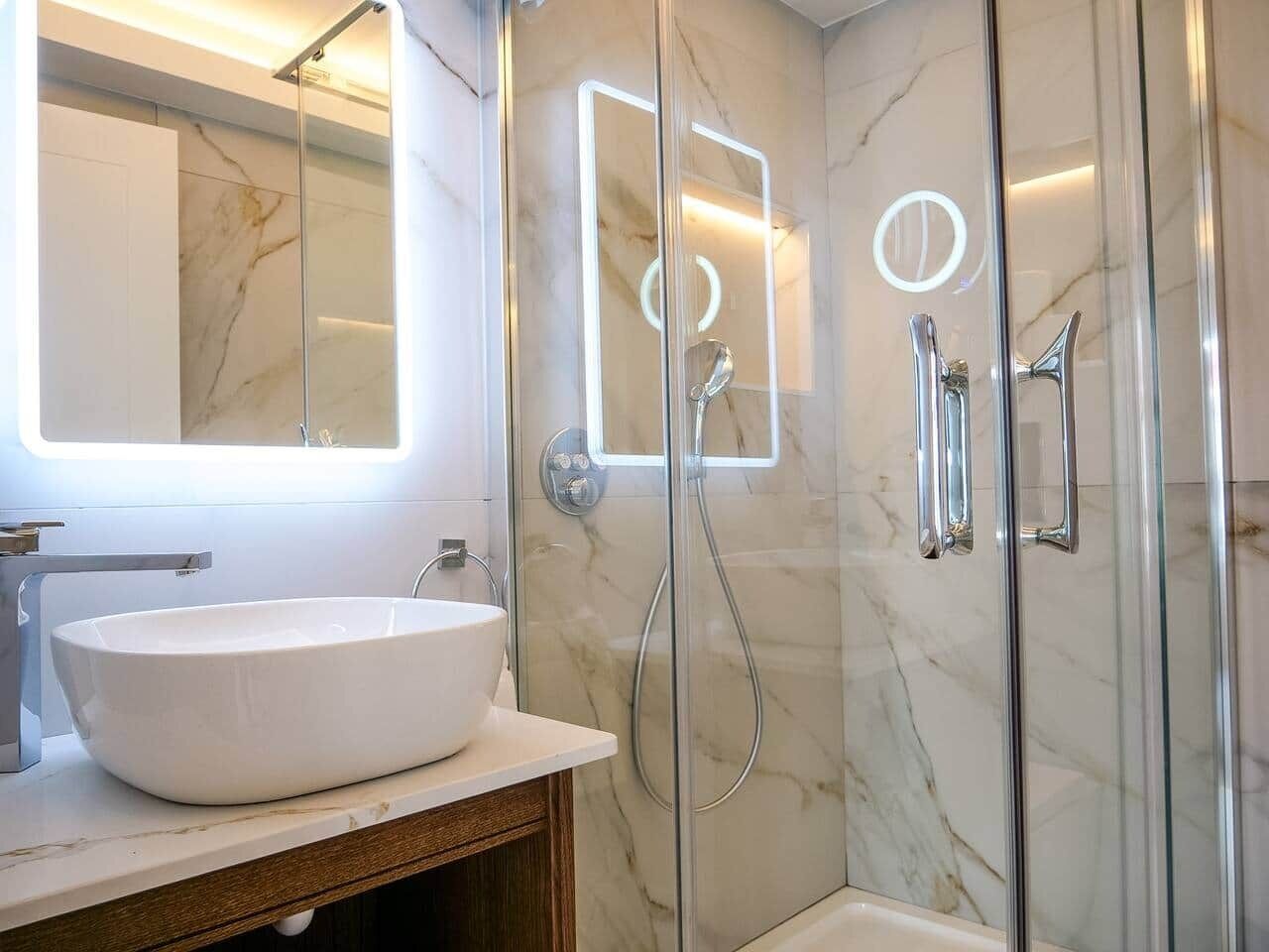 A modern bathroom with a white vessel sink, a glass shower enclosure, and a marble-tiled wall.