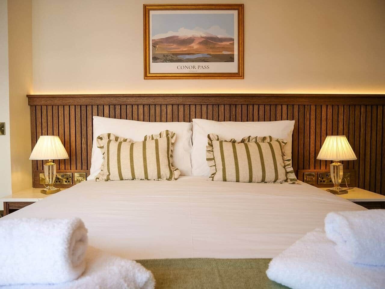 Une chambre d’hôtel avec un grand lit, deux lampes de chevet, un tableau encadré au mur et un lit soigneusement fait avec des serviettes.