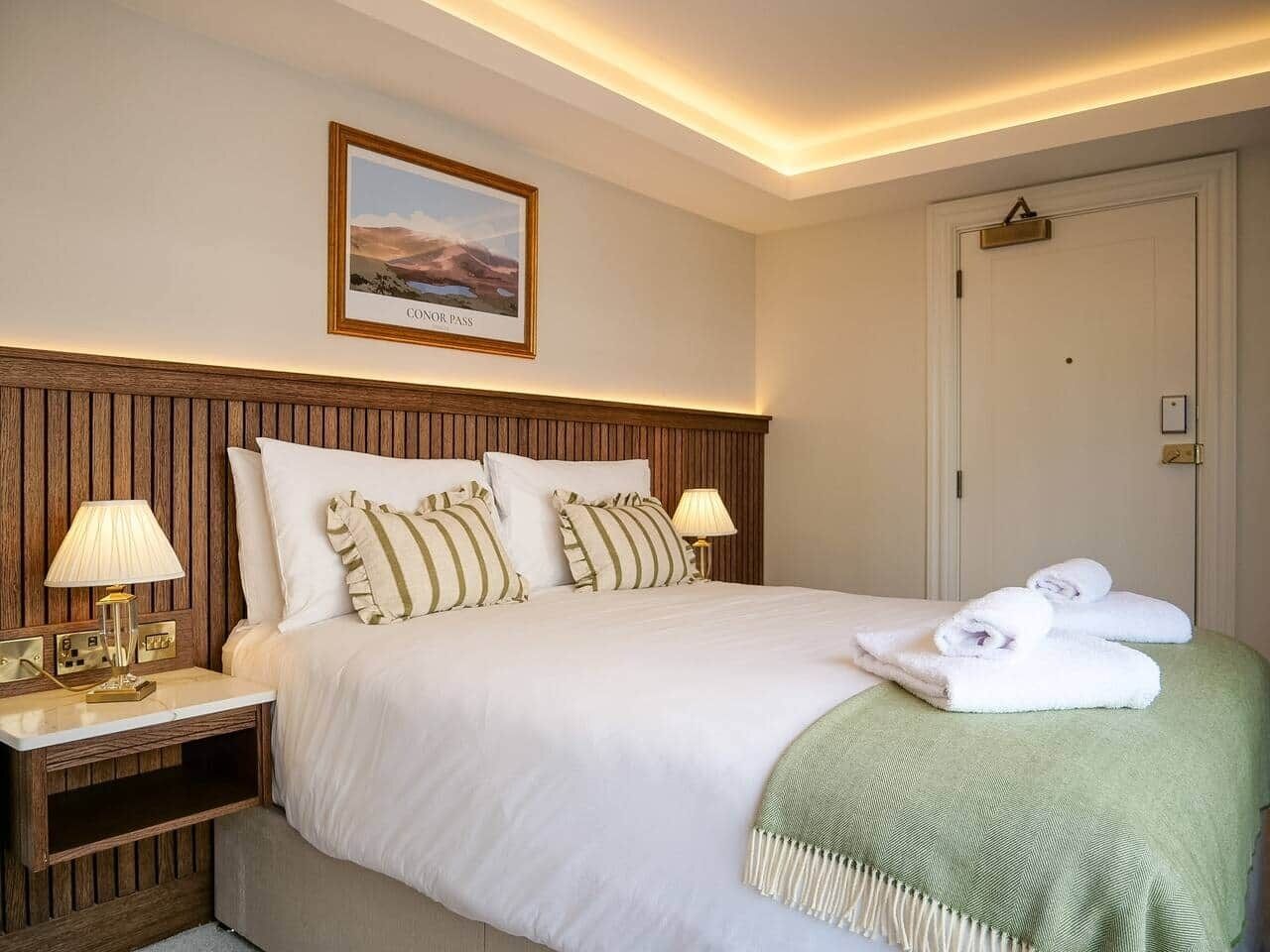 A hotel room with a bed, nightstands, lamps, a framed picture, and a door.
