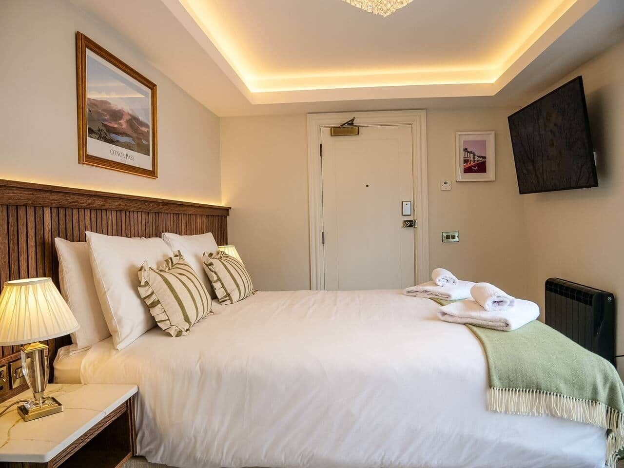 Une chambre d’hôtel avec un grand lit, une table de chevet avec une lampe, un téléviseur fixé au mur et une porte.