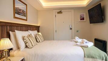 Une chambre d’hôtel avec un grand lit, une table de chevet avec une lampe, un téléviseur fixé au mur et une porte.