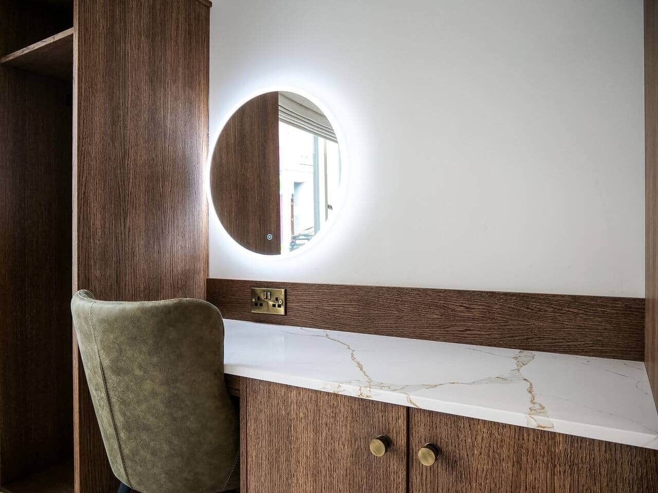 A bathroom with a wooden vanity, a round mirror, and a marble countertop.