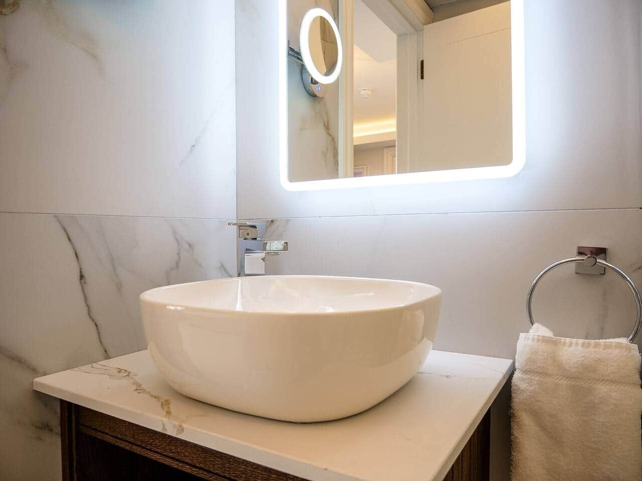 Une salle de bain avec un lavabo en marbre blanc, un miroir avec un éclairage intégré et un porte-serviettes.