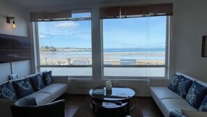 Un salón con sofá, mesa de centro y ventanas amplias con vista a la playa.