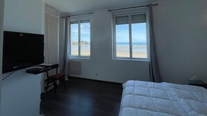 Una habitación con cama, televisión, ventana y vista a la playa, además de una silla.