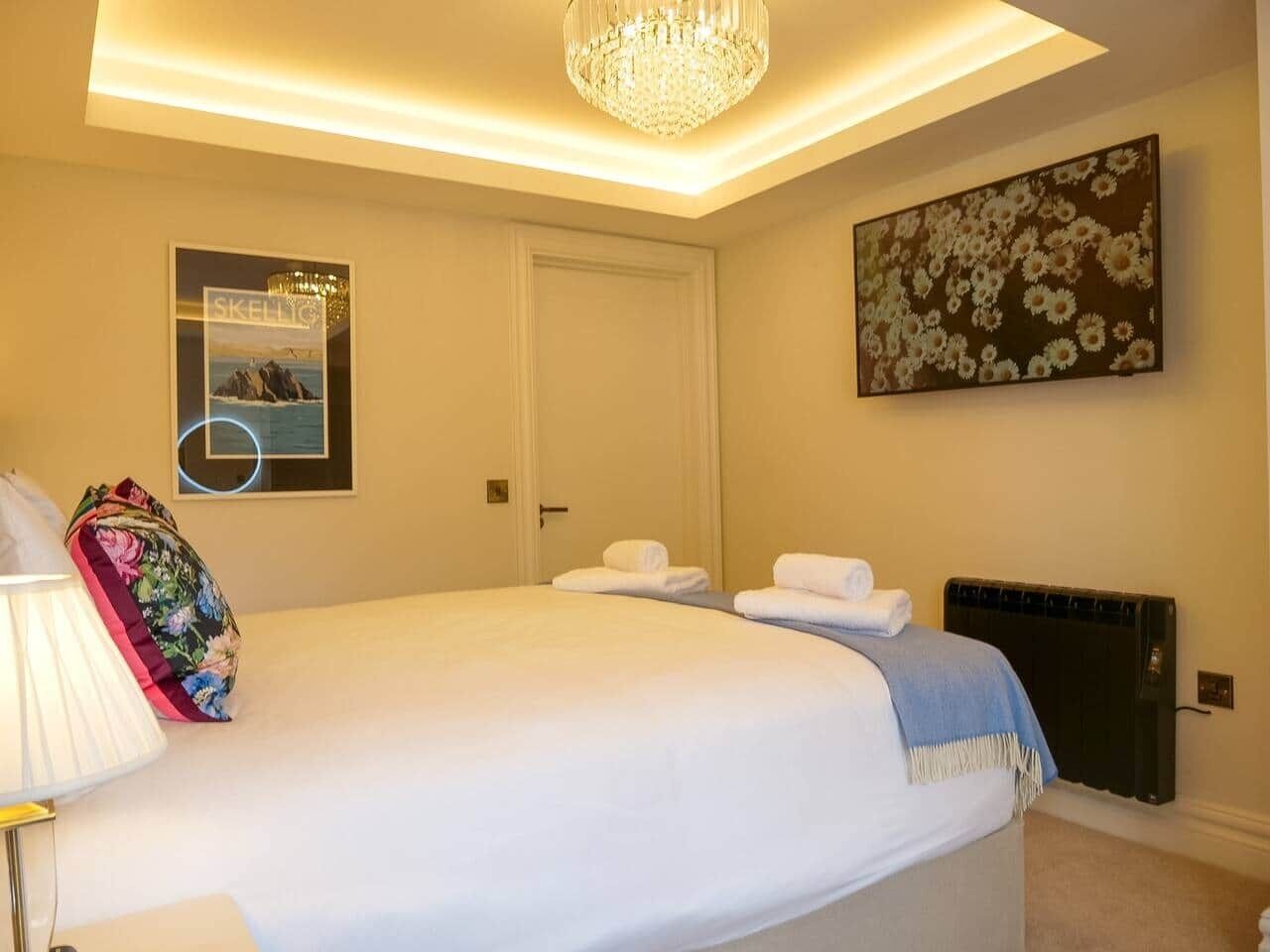 A hotel room with a bed, a radiator, a wall-mounted picture, and a chandelier.