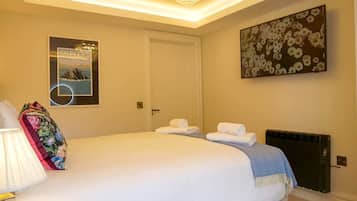 A hotel room with a bed, a radiator, a wall-mounted picture, and a chandelier.