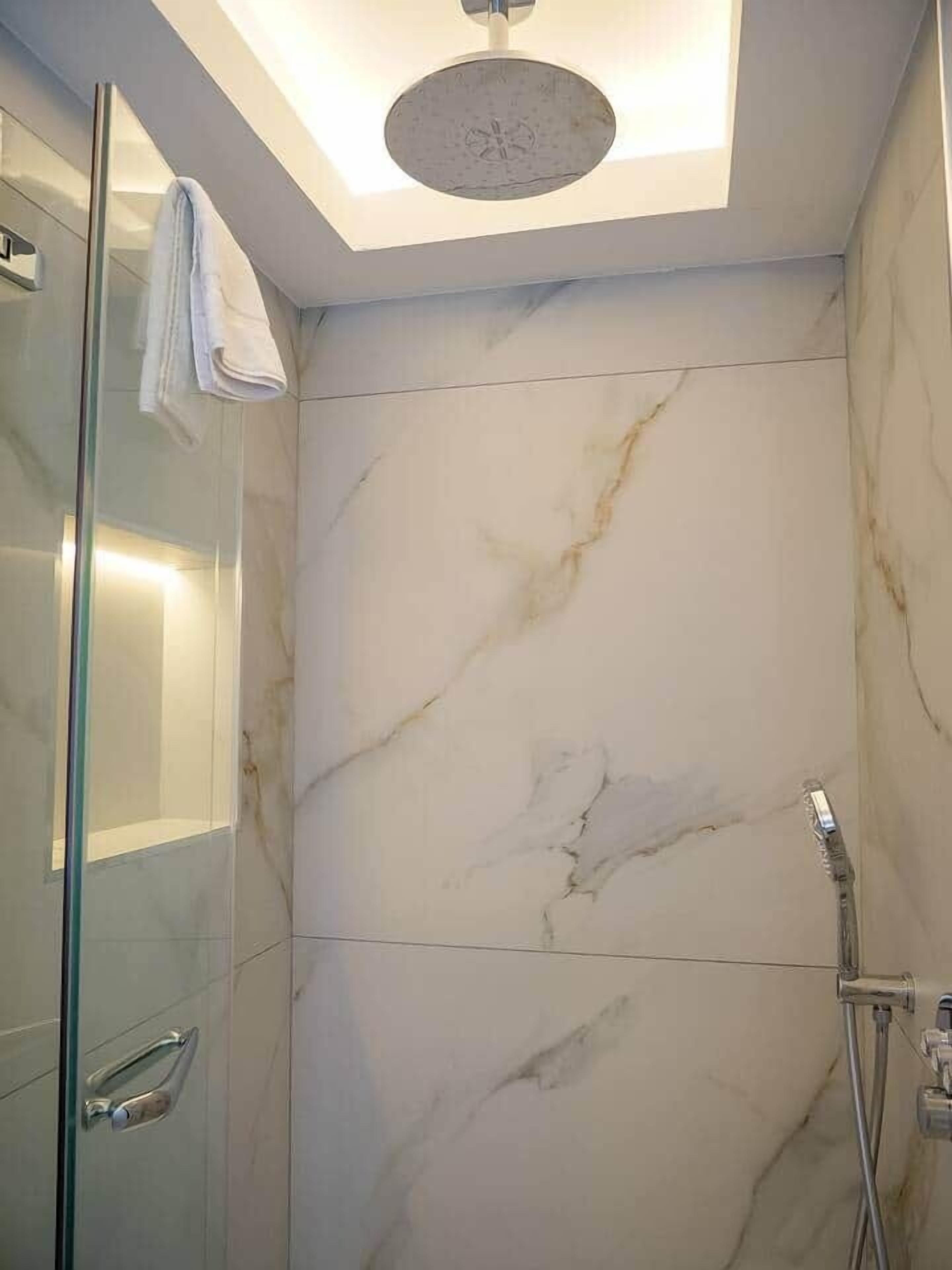 A modern bathroom with a glass shower enclosure, marble walls, and a ceiling light fixture.