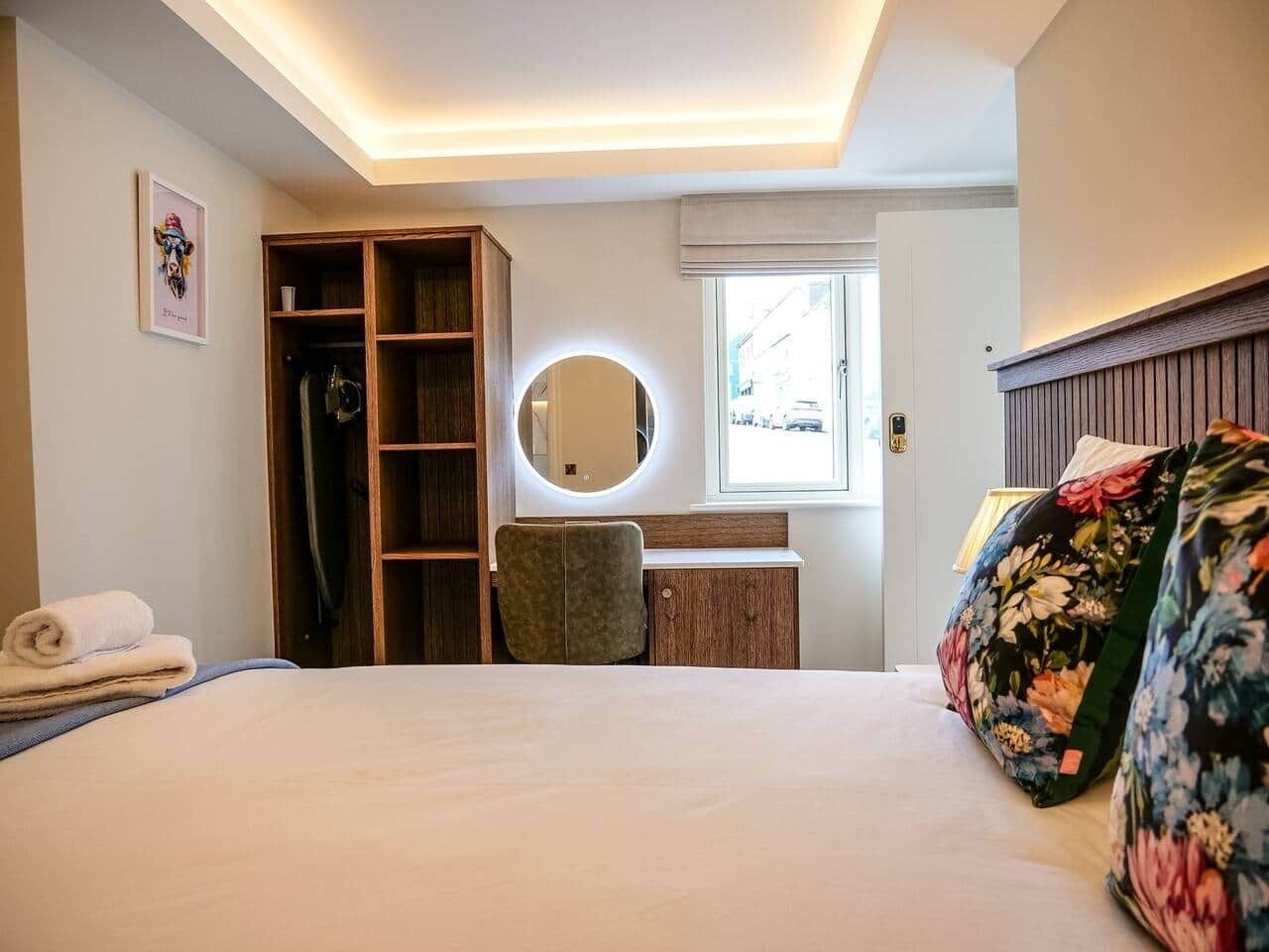 Una habitación de hotel con cama, armario, espejo, escritorio y ventana.