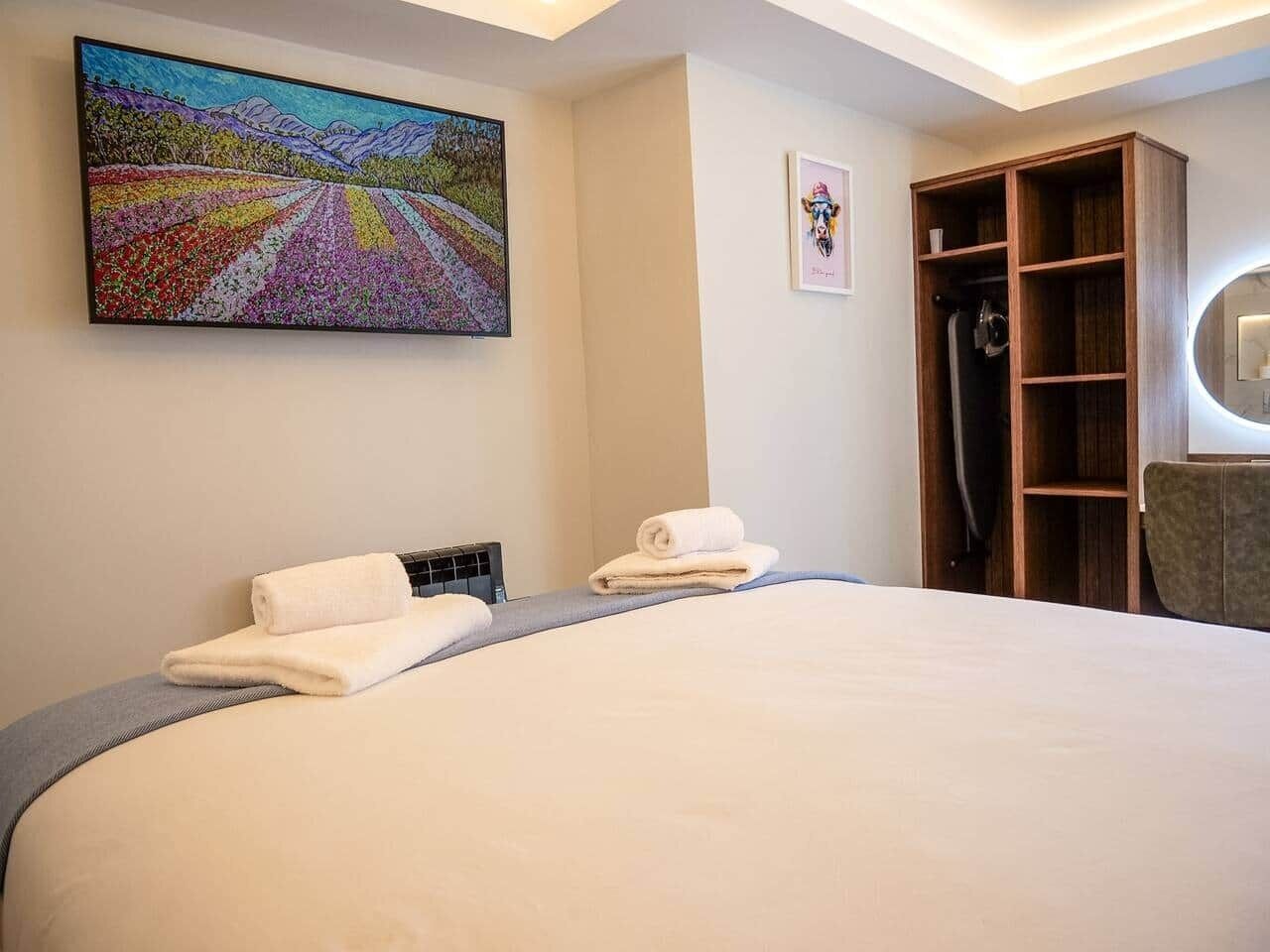Ein Hotelzimmer mit einem großen Bett, einem Bild an der Wand, einem Holzschrank und einem Spiegel.