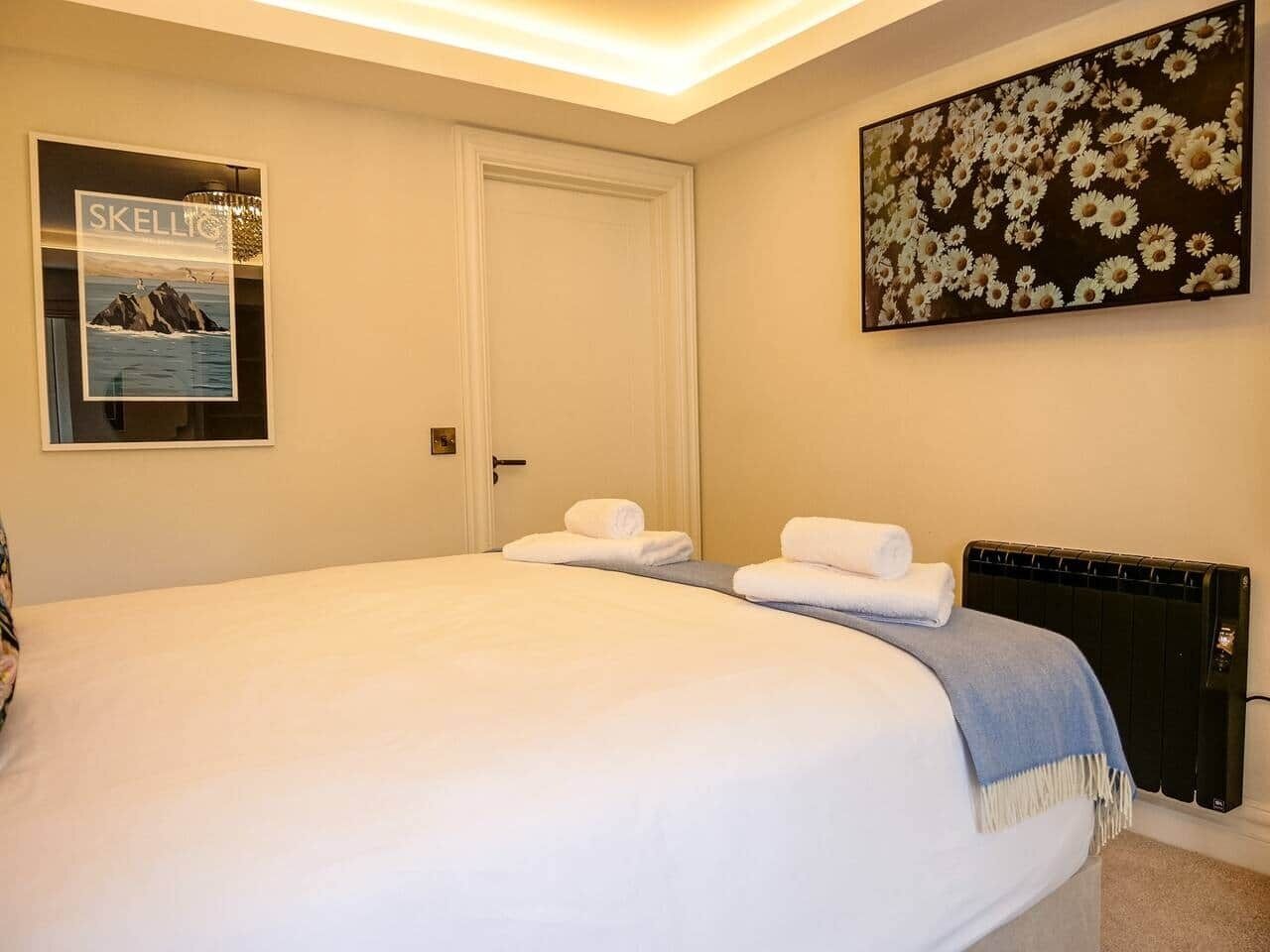 Een hotelkamer met een bed, een deur, een radiator en een muur met een bloemschilderij.