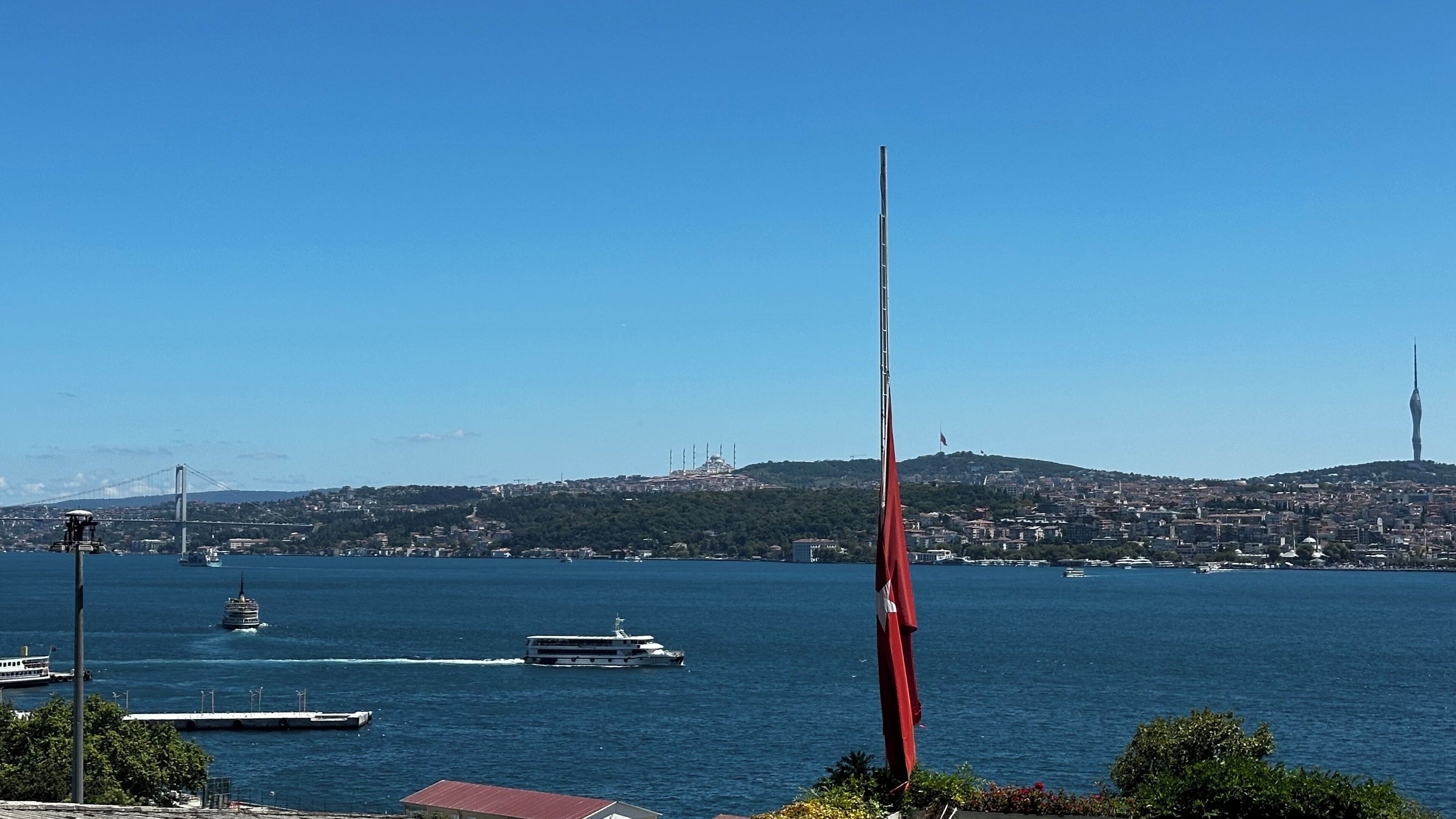 Eine Küstenstadtlandschaft mit einem markanten Turm, einer Brücke und einem Wasserabschnitt mit Booten.