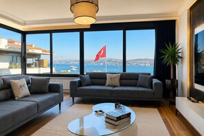 En moderne stue med en sofa, et glasbord og udsigt til havet med et flag.