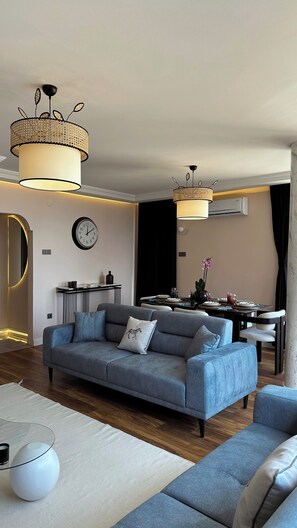 Ein modernes Wohnzimmer mit einer Couch, einem Essbereich mit gedecktem Tisch und einer großen Wanduhr.
