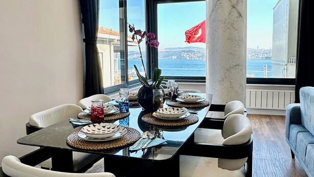 A dining area with a table set for four, a large window with a view of the sea, and a modern chandelier. - Serene Stylish Central Cihangir Flat w/ Bosphorus 3-bedroom apartment (Beyoglu)