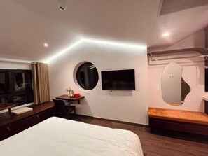 A modern hotel room with a large bed, a desk with a chair, a round mirror, a television, and a window with curtains. - Cocoon Danang Airport Hotel & Apartment (Da Nang)