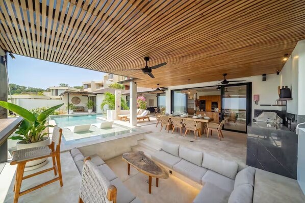 An outdoor living area with a pool, seating, and a ceiling fan. - Friendly Villa (Badung)