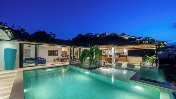 A modern pool area with glass walls, a seating area, and a view of the surrounding landscape. - Friendly Villa (Badung)