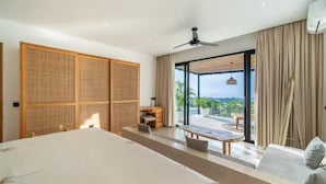 A modern hotel room with a large bed, a desk, a chair, a sofa, and a balcony with a view. - Friendly Villa (Badung)