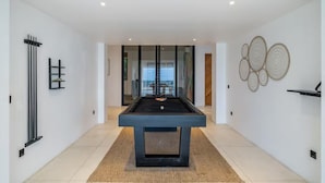 A modern room with a pool table, a glass door leading to a balcony, and decorative wall art. - Friendly Villa (Badung)