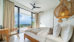 A bedroom with a bed, a desk, a chair, a ceiling fan, and a view through a glass door. - Friendly Villa (Badung)