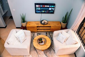 A living room with two sofas, a coffee table, a flat-screen TV, and potted plants.
