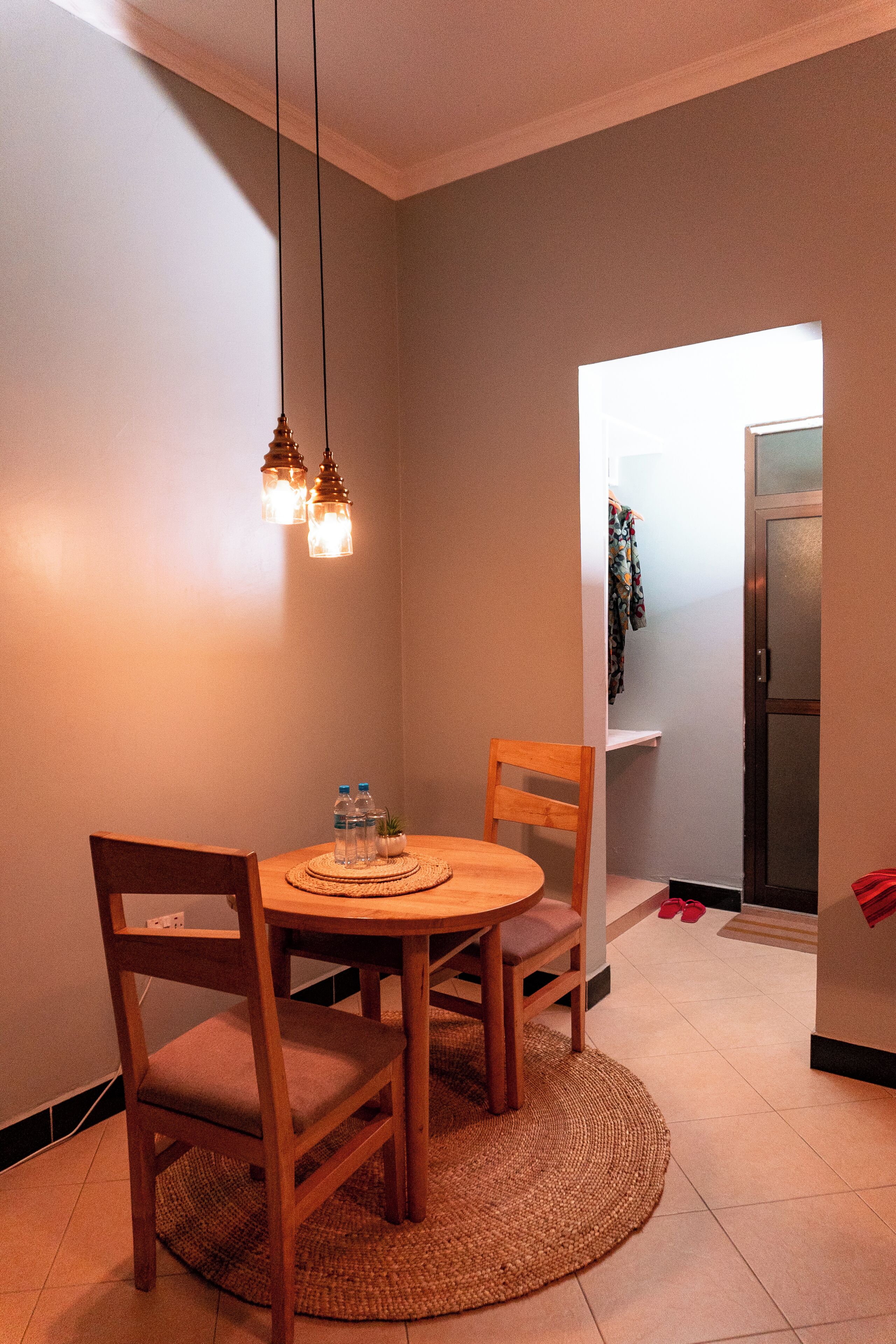 Comedor con una mesa redonda, dos sillas, un mantel tejido y lámparas colgantes.
