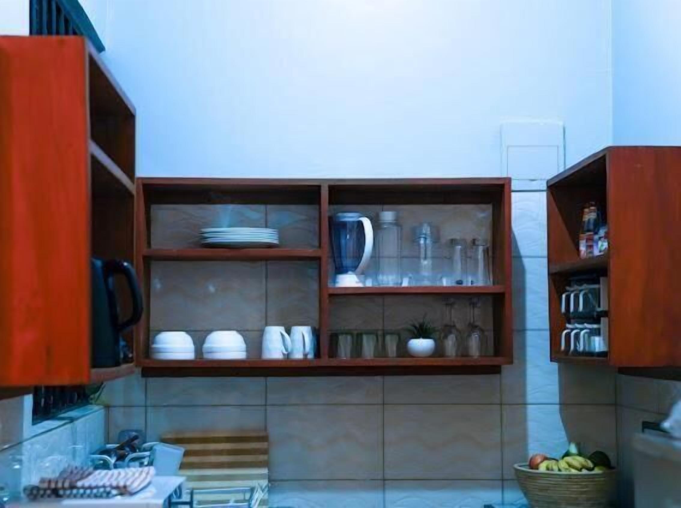 Una cucina con mobili in legno, mensole piene di stoviglie, un frullatore e un cesto di frutta.
