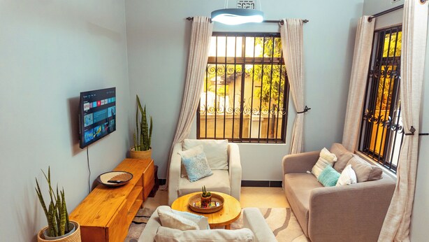 A living room with two sofas, a coffee table, a TV, and a window with curtains. - Ilboru Haven Homes (Arusha)